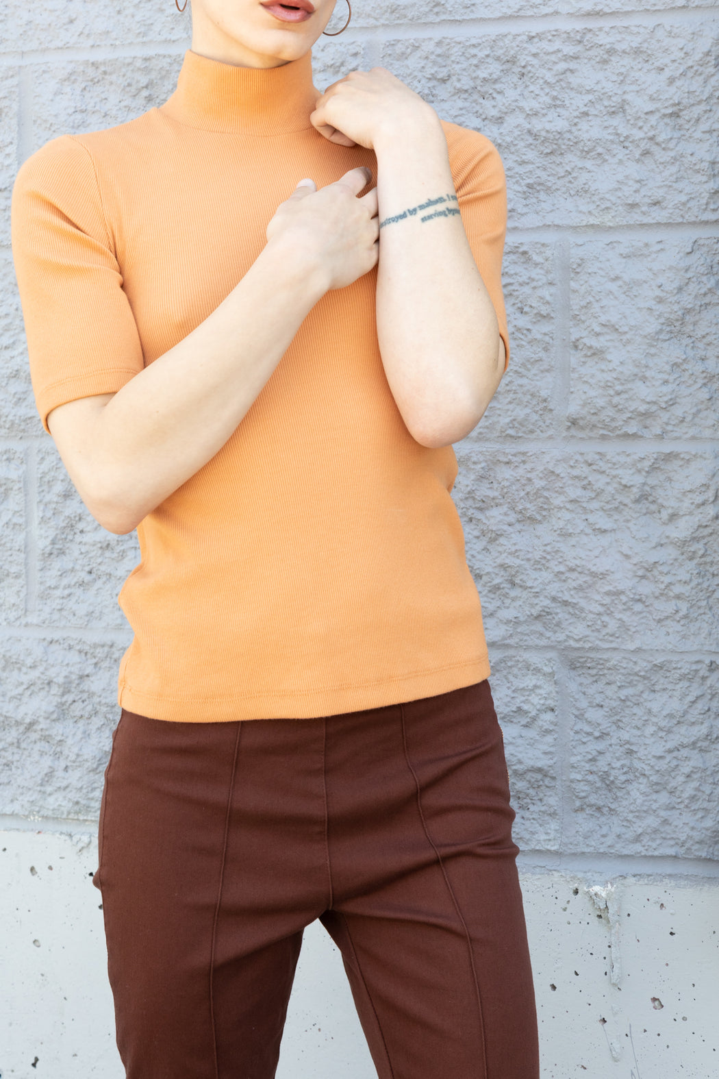 Photo of a sherbet orange, organic cotton tee in a thick rib with sleeves just above the elbow and a mock neck. Incredibly stretchy, it skims the body and holds its shape.
